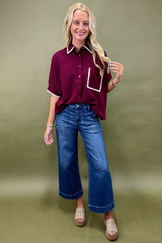 Woman wearing a maroon shirt with white trim and blue jeans on a green background