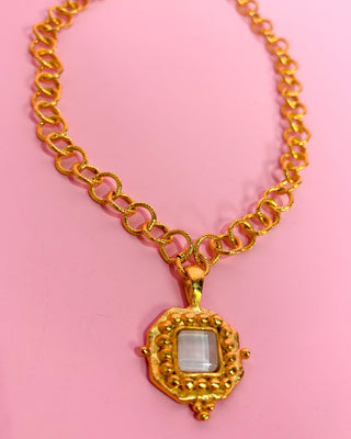 Gold chain necklace with a pendant on a pink background