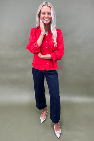 Woman wearing a red blouse and blue jeans against a plain background