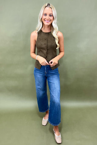 Woman wearing a green sleeveless top and blue jeans against a green background