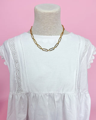 White dress with lace details on a mannequin against a pink background