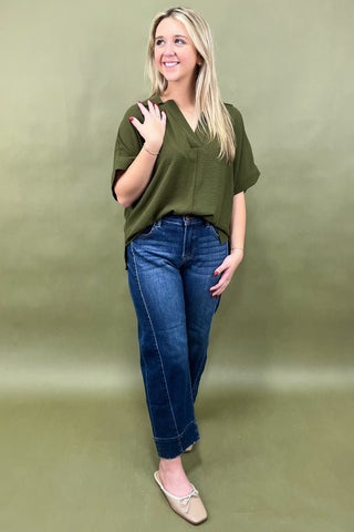 Woman wearing an olive green top and blue jeans against a green background