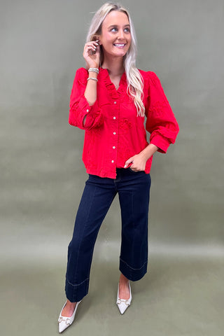 Woman wearing a red blouse and blue jeans against a plain background