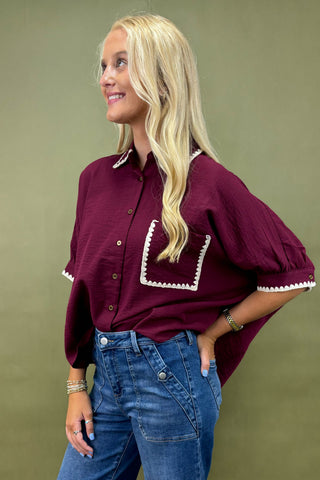 Woman wearing a burgundy blouse with white trim and blue jeans against a green background