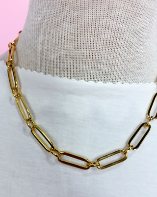 Gold chain necklace on a mannequin with a pink and white background