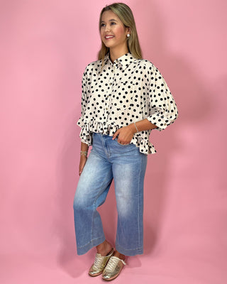Woman wearing a polka dot blouse and jeans against a pink background