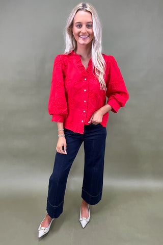 Woman wearing a red blouse and blue jeans against a plain background