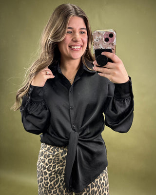 Woman taking a selfie with a phone, wearing a black shirt and leopard print pants on a green background