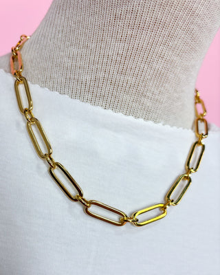 Gold chain necklace on a mannequin with a pink and gray background