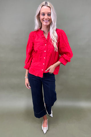 Woman wearing a red blouse and blue jeans against a plain background