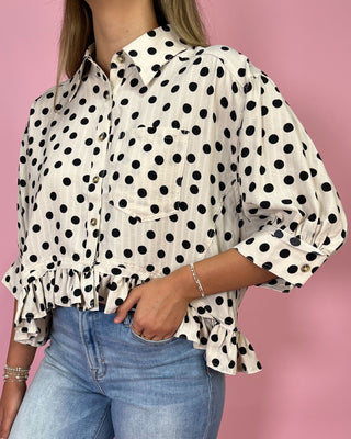 Person wearing a polka dot blouse with long sleeves and blue jeans against a pink background