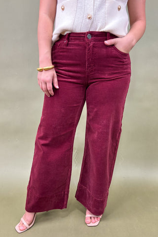 Person wearing maroon corduroy pants and a white top on a beige background