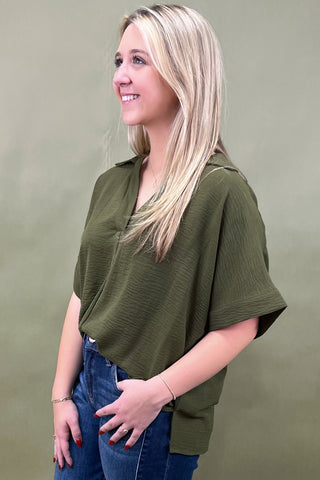 Woman wearing an olive green top and blue jeans against a green background