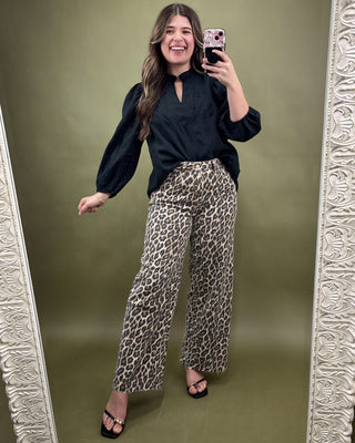 Woman taking a mirror selfie wearing a black top and leopard print pants on a green background