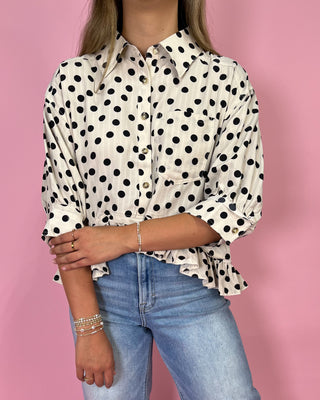 Person wearing a polka dot shirt and jeans against a pink background