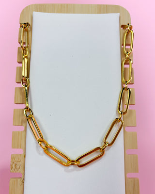 Gold chain necklace on a white card with a pink background