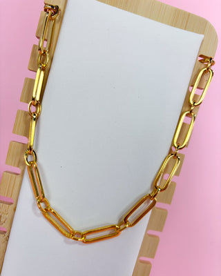 Gold chain necklace on a white card with a pink background