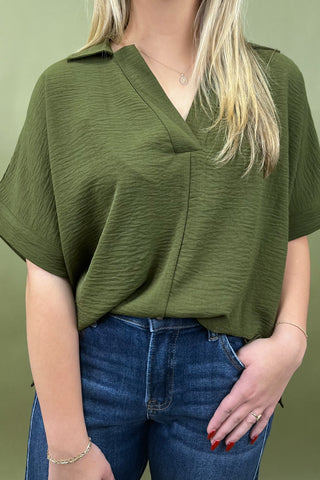 Person wearing a green top and blue jeans against a green background