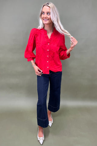 Woman wearing a red blouse and blue jeans against a plain background