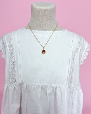 White dress with lace details on a mannequin against a pink background