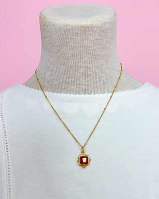 Gold necklace with a red pendant on a mannequin against a pink background