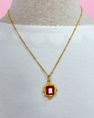 Gold necklace with a red pendant on a mannequin against a pink background