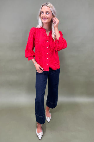 Woman wearing a red blouse and blue jeans against a plain background