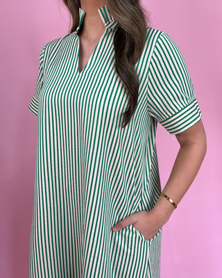 Green and white striped dress worn by a person on a pink background