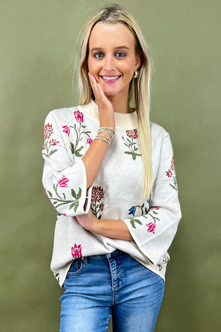 Woman wearing a white sweater with floral embroidery against a green background
