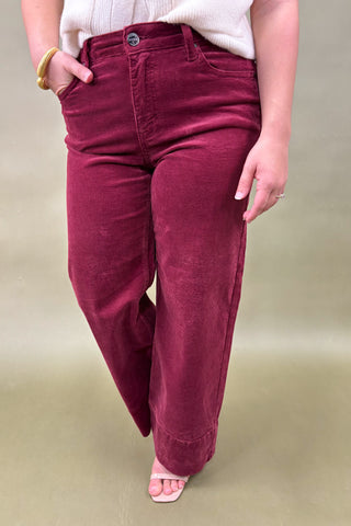 Maroon corduroy pants worn by a person on a beige background