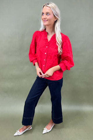 Woman wearing a red blouse and blue jeans against a plain background