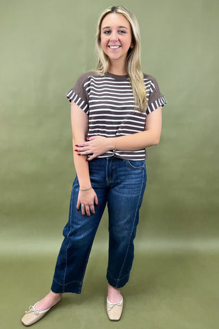Woman wearing a striped shirt and blue jeans against a green background