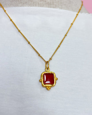 Gold necklace with a red pendant on a white background