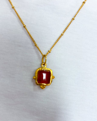 Gold necklace with a red pendant on a white background
