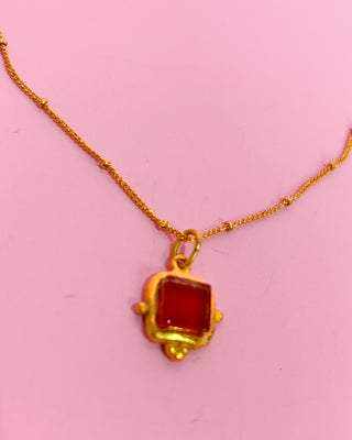 Gold necklace with a red pendant on a pink background