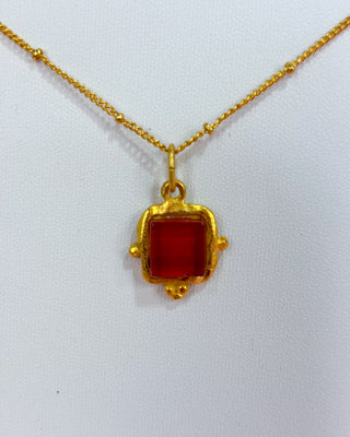 Gold necklace with a red square pendant on a white background