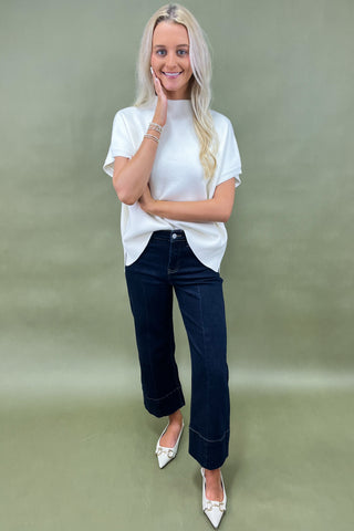 Woman wearing a white t-shirt and dark jeans on a green background