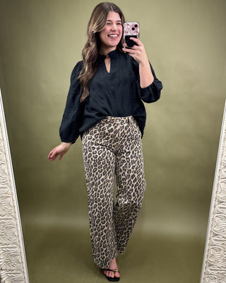 Woman taking a mirror selfie wearing a black top and leopard print pants on a green background