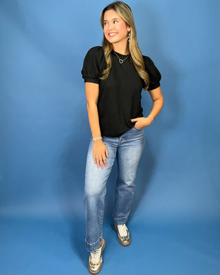A woman modeling a red ribbed short-sleeve top with puff sleeves, paired with blue jeans