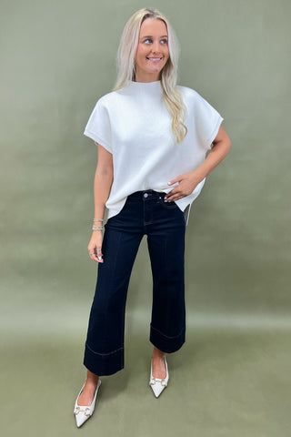 Woman wearing a white top and dark blue jeans against a green background