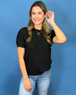 A woman modeling a red ribbed short-sleeve top with puff sleeves, paired with blue jeans