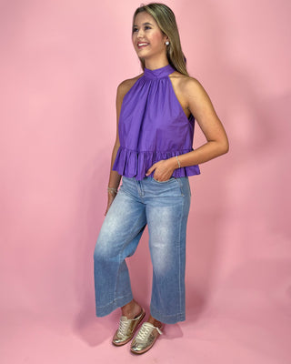 Woman wearing a purple top and blue jeans against a pink background