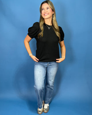 A woman modeling a red ribbed short-sleeve top with puff sleeves, paired with blue jeans
