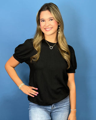 A woman modeling a red ribbed short-sleeve top with puff sleeves, paired with blue jeans
