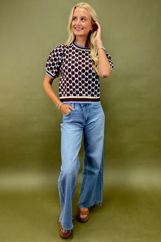 Woman wearing a patterned top and blue jeans against a green background