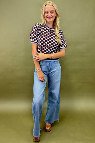 Woman wearing a patterned shirt and blue jeans against a green background