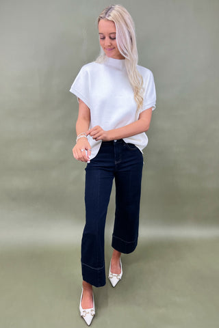 Woman wearing a white top and dark jeans on a plain background