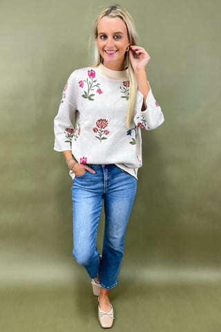 Woman wearing a white floral embroidered top and blue jeans on a green background