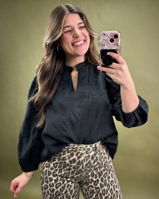 Woman taking a selfie with a phone, wearing a black top and leopard print pants on a green background