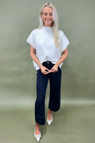 Woman wearing a white top and dark blue jeans against a green background